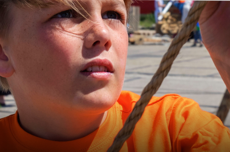 Close-up van een blonde jongen met een oranje shirt spelend op een zonnig schoolplein