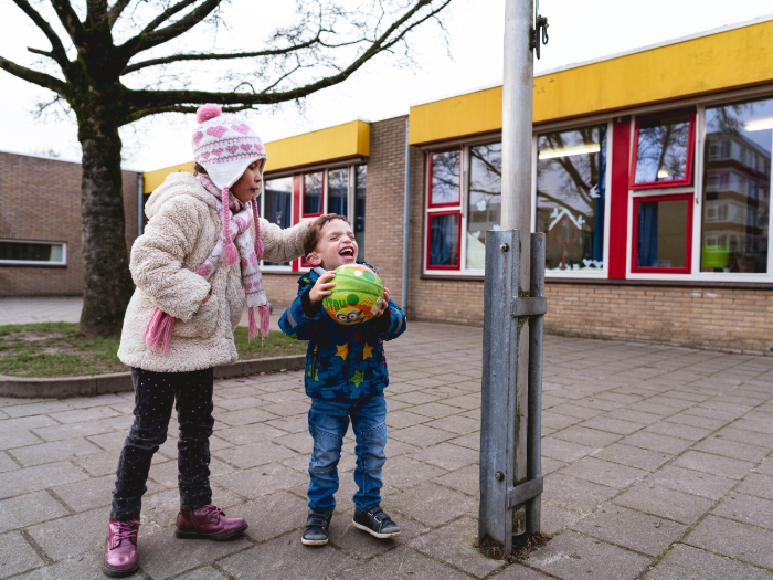 Sfeerbeeld van twee kinderen die op een schoolplein met een bal spelen