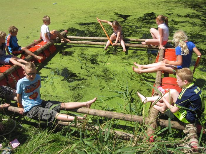 Sfeerbeeld van acht kinderen op een groot vlot in een kroosrijke sloot op een mooie zomerdag