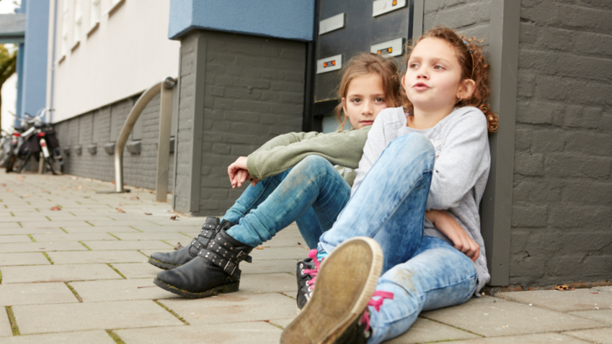 Kinderen zitten op de stoep. Wij raden het speeltuinen aan te werken met een meldcode huiselijk geweld en kindermishandeling - Jantje Beton