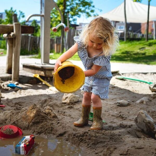 Een kindje gooit zand uit een emmer. Het is belangrijk om erkenning en financiering van gemeenten te krijgen voor speeltuinen - Jantje Beton